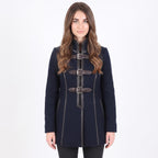 A woman modeling a dark navy blue coat with brown leather-like doggle straps and silver buckles, set against a plain white studio background.